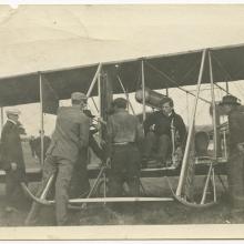 Harry Bingham Brown, a white male pilot, prepares for takeoff in his Wright biplane with the help of several other men.