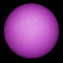 Purple disk view of the Sun's chromosphere featuring darker spots called sunspots and phages, or lighter clouds, across the visible section of the Sun.