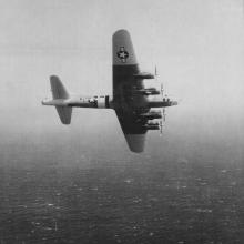 View of a U.S. military monoplane during a test flight over an ocean.