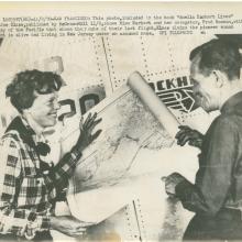 Amelia Earhart, a white female pilot, and Fred Noonan, a white male navigator, stand together looking at a map. A caption suggests a different ending to the flight that led to Earhart's disappearance.