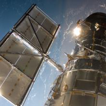 Partial view of the Hubble Space Telescope, a large telescope with two sets of solar panels (one on each side), from the perspective of the Space Shuttle Atlantis.