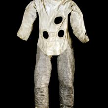 Front view of astronaut suit used for astronaut training on Earth. The top half features a white fabric with multiple holes representing life support tubes, whereas the bottom half features a silver-colored fabric.