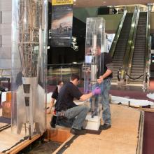 Three Museum staff members work to remove a primitive rocket from a protective case prior to transporting the rocket.