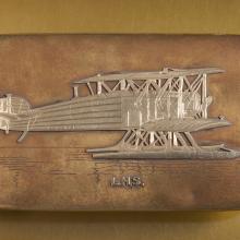 Top of golden box-shaped case featuring an engraved golden biplane.