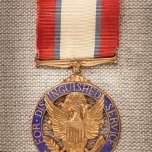 Purple and gold-colored metal medal with red, white, and blue-stripped ribbon. Front of medal features an eagle crest.