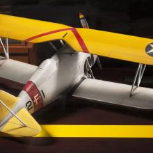 Back view of yellow and silver-colored biplane model aircraft. One white star inside a blue circle is featured on both sides of the top wing.