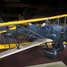 Side view of gray biplane model aircraft with yellow and silver-colored wings and one propellor.