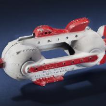 Side view of white attacking spaceship toy with center opening between two spherical sides of the ship. Ship features red fins, nose, and propellor.