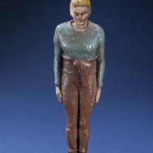 Front view of person-shaped statuette with blue-gray top and brown pants. "Flash Gordon" is painted in black on the front of the base.