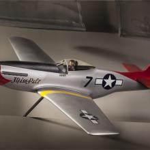 Side view of silver-colored monoplane model aircraft with one engine and a red tail and nose. Blue and white star emblem is painted on the rear of the fuselage and on the left wing.