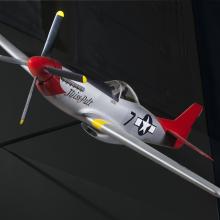 Frontal side view of silver-colored monoplane model aircraft with one engine and a red tail and nose. Blue and white star emblem is painted on the rear of the fuselage.