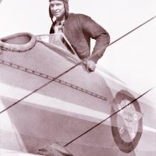 Earl W. Renfroe, an African-American male pilot, stands in the cockpit of a biplane.