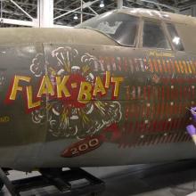 A member of the Museum's conservation staff works to conserve a portion of an olive drab green bomber aircraft from World War II.