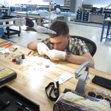 A white, male professional watchmaker closely inspects a watch.