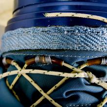 Close-up view of developmental blue glove. Thin, tan rope acts as a lacing system under a blue skirt.