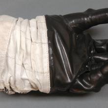 Left glove to astronaut suit. Black-colored rubber palm and fingertips section attached to a white fabric. The white fabric is attached to a solid blue disconnect from the rest of the suit.