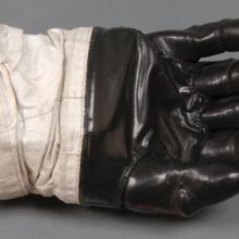 Right glove to astronaut suit. Black-colored rubber palm and fingertips section attached to a white fabric. The white fabric is attached to a solid red disconnect from the rest of the suit.