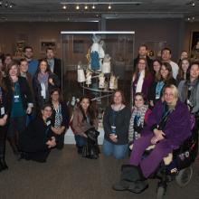 A group of people pose together around an artpiece made from various astronaut gloves.