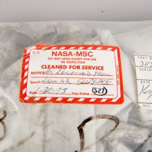 Cover of a sealed white-colored fabric cover for an oxygen purge system. One red and white tag states that the cover has been "cleaned for service" and is not to be opened "except for use or inspection".