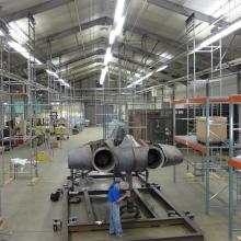 A Museum staff member is securing a gray-colored metal aircraft to a steel stand.