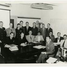 A group of men pose formally during a meeting to discuss spacecraft.