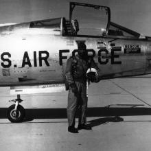 Major Robert Lawrence, an African-American male pilot and pilot, poses outside of an aircraft in aviation gear. He is holding his helmet.