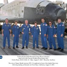 The seven members of the Space Shuttle mission STS-114 stand in front of the Space Shuttle Discovery for a group photo in their blue flight gear.