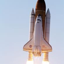 Space Shuttle Discovery, a plane-like object used in space which is attached to three large rockets, is soaring in the atmosphere towards space.