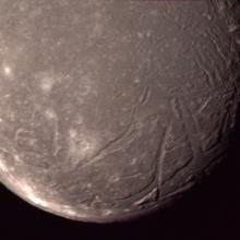 A close-up view of Ariel, a moon of Uranus, and some of its terrain with large craters creating lines