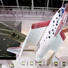 A red, white, and blue rocket-shaped spacecraft with foldable wings displayed inside the National Air and Space Museum.