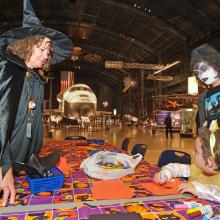 Trick-or-treater vistors stand at a Halloween-themed display with a museum curator dressed in a witch costume.