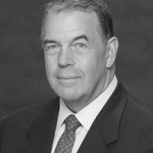 Black and white portrait of David C. Hurley, a former president of the National Air and Space Museum Board, who smiles towards the subject