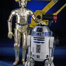 R2-D2, a blue and white robot "droid" from the Star Wars franchise, and C-3PO, a golden-metalic robot "droid" from the Star Wars franchise, stand next to each other on display at the museum.