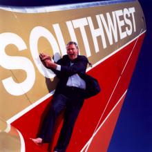 Herb Kelleher, a white man, lies next to an aircraft wing with Southwest livery