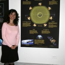 A college student stands to the side of their banner discussing social uses of GPS technology