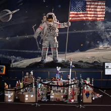 A finished view of a space station project completed by museum patrons below a mural of a man on the moon.