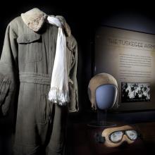 Flight suit, scarf, helmet, and goggles displayed next to Tuskegee Airmen graphic