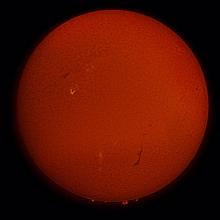 Disc view of full sphere of Sun with a brighter patch of gases seen from the telescope on the left side.