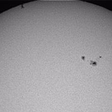 A partial view of the Sun as the International Space Station, a set of dots on the upper left side of the photo, transits the Sun.