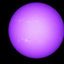 Disk view of the Sun with visible sunspots on the left side of the visible surface.