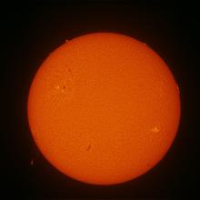 Disk view of the Sun with one faint prominence visible on the bottom left quadrant of the disk.