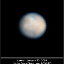 A round-shaped, gray and tan asteroid with multiple visible craters.