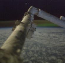 A large, arm-like object on the International Space Station in front of the Aurora Borealis in the background.