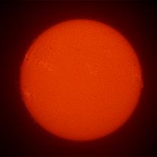 Disk view of the Sun with a large sunspot cluster visible on the left side of the Sun. 