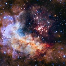 A nebula of dust and gases with orange, red, and pink clouds visible. Several blue and red starts are also visible.