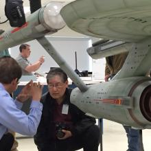 Multiple Museum staff members in charge of a gray spaceship studio model from the series Star Trek tour the Museum's conservation laboratory, where the studio model is undergoing conservation treatments.