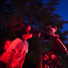 A young person looks through a telescope during a nighttime observing event.