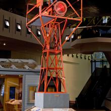 Orange, metal structure holding rotating light used for air travel. Structure is displayed in the Museum.