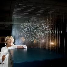 Angela Palmer, a white woman, stands next to the installation of her glass sculpture highlighting the findings of the Kepler Space Telescope.