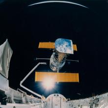 The Hubble Space Telescope, a large telescope with a set of solar panels on two sides, is deployed from the Space Shuttle Discovery.